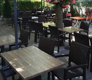 Terrasse bei Tag mit Tischen unter einem Baum, Hängeblumen und Laternen